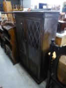 AN OAK TWO DOOR BOOKCASE WITH LEADED GLASS PANELS OVER LINEN FOLD DECORATION