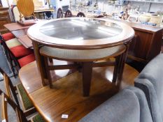 A TEAK CIRCULAR COFFEE TABLE WITH SMOKED GLASS TOP AND THREE QUADRANT SHAPED NESTING TABLES