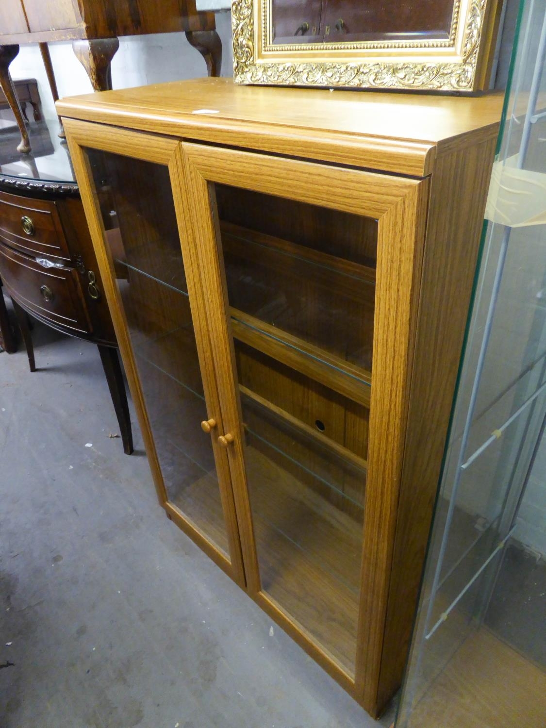 A WOOD EFFECT SMALL BOOKCASE, ENCLOSED BY TWO GLAZED DOORS