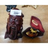 A SMALL ORIENTAL CARVED WOOD MASK HEAD WALL ORNAMENT AND A SMALL MEERSCHAUM PIPE BOWL SURMOUNTED