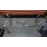 A MODERN OBLONG COFFEE TABLE WITH PLATE GLASS TOP, ON CONTINUOUS BRIGHT METAL END SUPPORTS