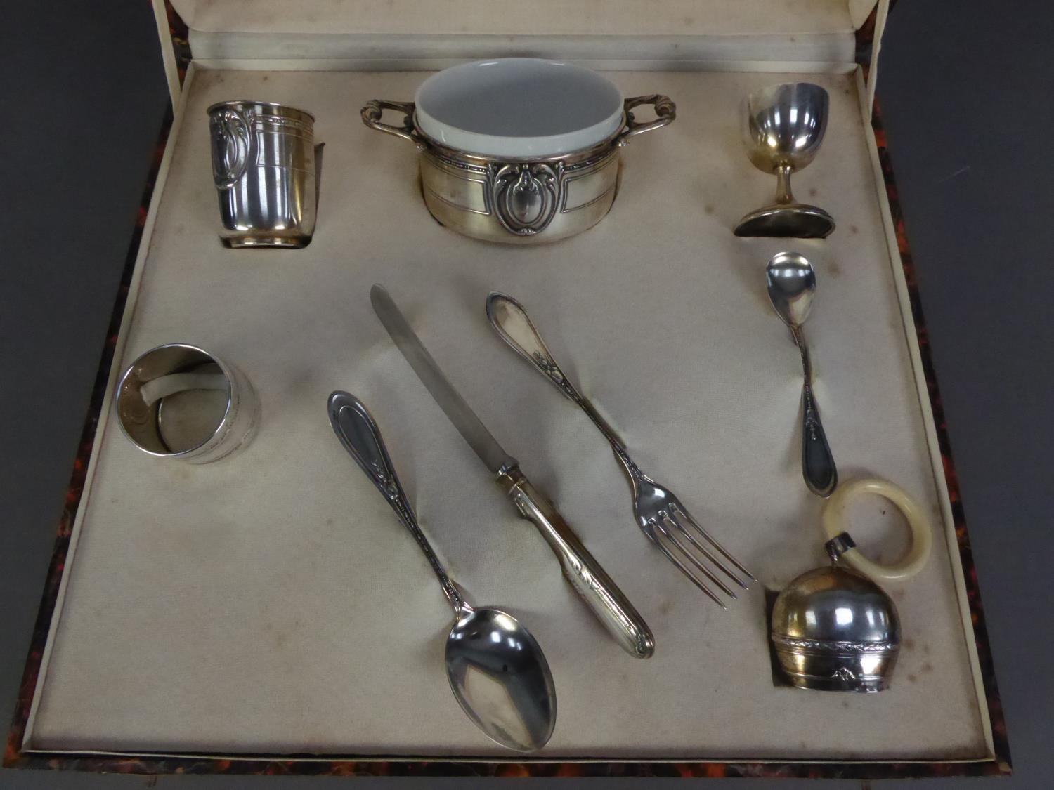 CASED NINE PIECE EMBOSSED FOREIGN SILVER COLOURED METAL CHRISTENING SET, RETAILED BY NICOLO