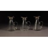 GEORGE V SET OF THREE CONICAL GLASS SMALL JUGS WITH SILVER COLLARS AND LIDS, star cut bases and loop