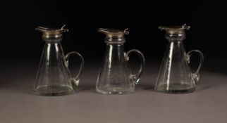 GEORGE V SET OF THREE CONICAL GLASS SMALL JUGS WITH SILVER COLLARS AND LIDS, star cut bases and loop