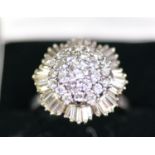 WHITE GOLD COLOURED METAL (unmarked) AND DIAMOND CLUSTER RING with domed three tier centre, the