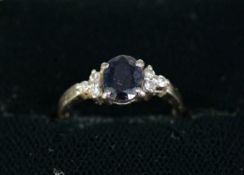 18ct WHITE GOLD RING, set with an oval dark blue sapphire and a trio of small diamonds to each