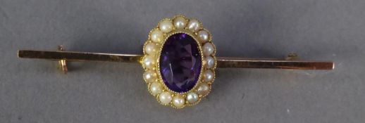 A GOLD COLOURED METAL BAR BROOCH, set with centre oval cluster with oval amethysts and surround of