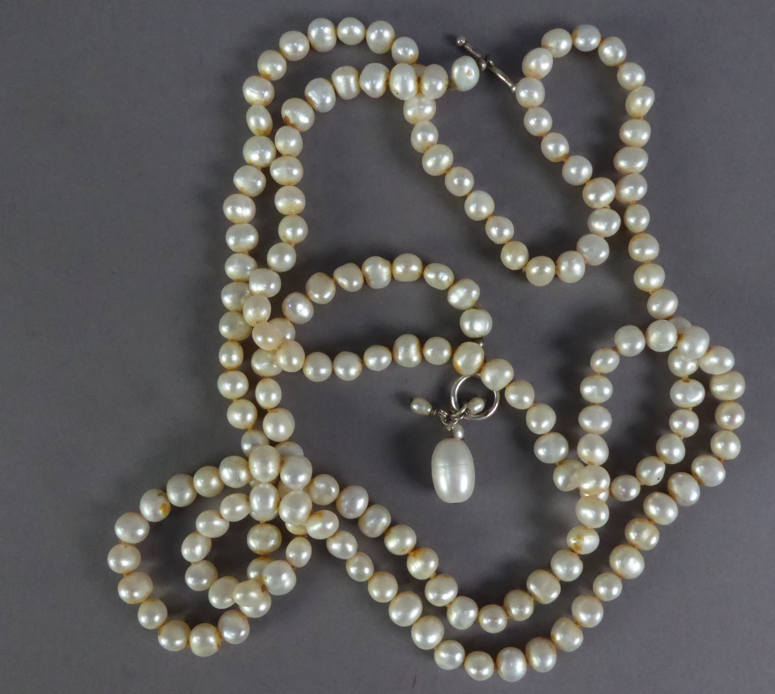 LONG, SINGLE STRAND NECKLACE OF CULTURED BAROQUE PEARLS of roughly uniform size, with metal ring and