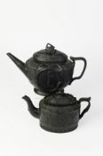 TWO NINETEENTH CENTURY MOULDED BLACK BASALT POTTERY TEAPOTS AND COVERS, one of oval footed form with