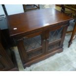 A CARVED MAHOGANY SMALL CUPBOARD ENCLOSED BY TWO LEAD LIGHT GLAZED DOORS WITH CARVED LOWER PANELS (