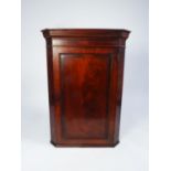 EARLY NINETEENTH CENTURY FIGURED MAHOGANY CORNER CUPBOARD, the moulded cornice above a flame cut and