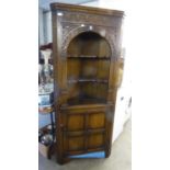 A CARVED OAK DOUBLE CORNER CUPBOARD WITH OPEN SHELVES OVER A CUPBOARD