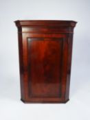 EARLY NINETEENTH CENTURY FIGURED MAHOGANY CORNER CUPBOARD, the moulded cornice above a flame cut and