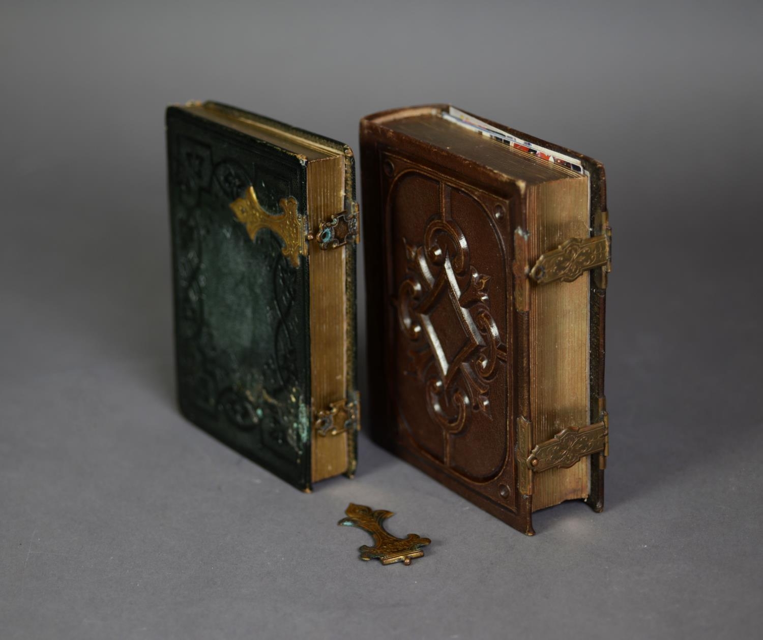 TWO EDWARDIAN BOOK PATTERN SMALL PHOTOGRAPH ALBUMS, each with embossed leather boards, gilt metal