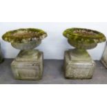 PAIR OF RECONSTITUTED STONE GARDEN URNS of shallow circular form, with moulded turned-over borders