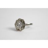 WHITE GOLD COLOURED METAL (unmarked) AND DIAMOND CLUSTER RING with domed three tier centre, the