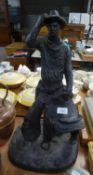 A LARGE BLACK COMPOSITION FIGURE OF A COWBOY STANDING HOLDING HIS SADDLE, ON OVAL BASE, 22? HIGH