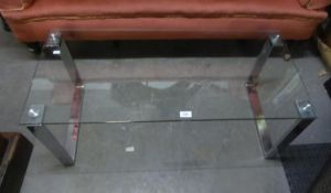 A MODERN OBLONG COFFEE TABLE WITH PLATE GLASS TOP, ON CONTINUOUS BRIGHT METAL END SUPPORTS