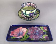 MOORCROFT POTTERY TEACUP AND SAUCER with tube lined radiating decoration of purple formal flowers