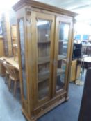 A LARGE PINE TWO DOOR GLAZED BOOKCASE WITH SINGLE DRAWER ON BUN FEET