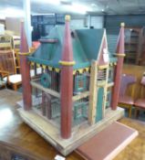 A PAINTED WOOD SQUARE BIRD CAGE IN THE FORM OF A BUILDING WITH A PITCH ROOF AND CORNER TURRETS, WITH