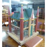 A PAINTED WOOD SQUARE BIRD CAGE IN THE FORM OF A BUILDING WITH A PITCH ROOF AND CORNER TURRETS, WITH
