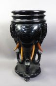 ORIENTAL CARVED AND EBONISED WOOD URN STAND, raised on three bulky elephant head supports to a