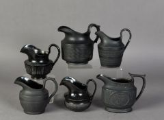 FOUR NINETEENTH CENTURY BLACK BASALT POTTERY MILK JUGS, three with engine turned decoration, the