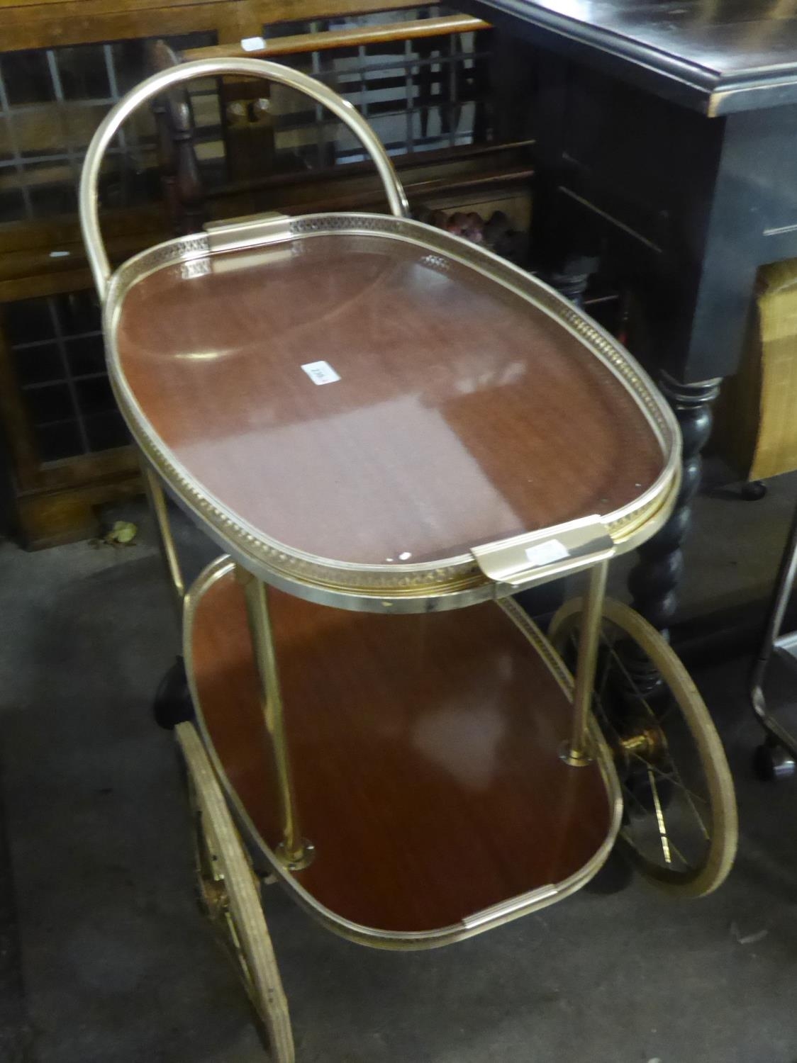 A GILT METAL TWO TIER COCKTAIL TROLLEY, WITH LARGE AND SMALL WHEELS, WOOD EFFECT FORMICA TOPPED
