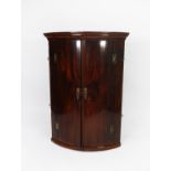GEORGE III FIGURED MAHOGANY BOW FRONTED CORNER CUPBOARD, of typical form with four spice drawers and