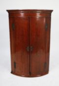 GEORGE III ’PLUM PUDDING’ MAHOGANY BOW FRONTED CORNER CUPBOARD, of typical form with dentil