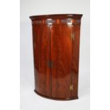 GEORGE III INLAID AND FLAME CUT MAHOGANY BOW FRONTED CORNER CUPBOARD, of typical form with three