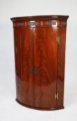 GEORGE III INLAID AND FLAME CUT MAHOGANY BOW FRONTED CORNER CUPBOARD, of typical form with three