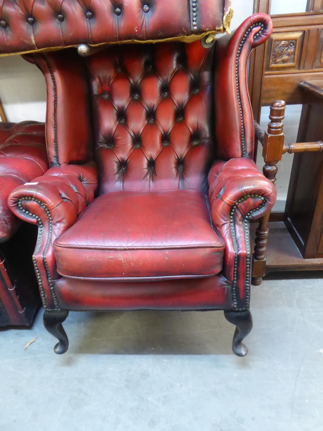 A CHESTERFIELD WING BACK QUEEN ANNE STYLE HIGH-BACK FIRESIDE ARMCHAIR, COVERED IN OX-BLOOD