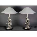 TWO CASED SILVER FIGURAL BEDSIDE LAMPS, in the form of a young woman seated on a wall reading to a