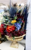 DISPLAY OF MULTI- COLOURED ARTIFICIAL FLOWERS AND FEATHERS IN A GILT PLASTIC CAMPANA URN SHAPED