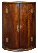 A George III oak bow fronted hanging corner cupboard