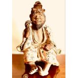 TERRACOTTA AND GLAZED JAPANESE SEATED FIGURE HOLDING A GILDED FISH AND SURMOUNTED BY AN OPEN-MOUTHED