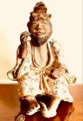 TERRACOTTA AND GLAZED JAPANESE SEATED FIGURE HOLDING A GILDED FISH AND SURMOUNTED BY AN OPEN-MOUTHED