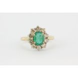 A hallmarked 14ct yellow gold cluster ring set with an oval cut emerald surrounded by brilliant