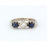 An 18ct white gold ring set with a princess cut diamond flanked by oval cut sapphires, (O.5),