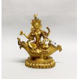 A Tibetan gilt bronze figure of a four armed goddess seated on a mythical sea creature, H. 26cm.