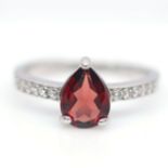 A 925 silver solitaire ring set with a pear cut garnet and white stone set shoulders, (K). Condition