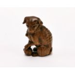 A carved fruitwood Netsuke of a dog with a ball with black obsidian eyes, H. 5cm.