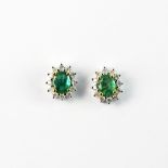 A pair of white metal (tested 14ct gold) cluster earrings set with oval cut emeralds and brilliant
