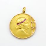 An 18ct yellow gold Art Nouveau pendant of a lady set with round cut rubies, dia. 3cm.
