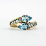 A 9ct yellow gold (stamped 9k) crossover ring set with pear cut blue topaz, diamonds and blue