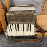 A vintage Alvari piano accordion with a case of sheet music.