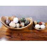 A collection of polished stone eggs with one wooden egg and two polished wooden bowls.