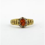 A hallmarked 18ct yellow gold cluster ring set with an oval cut synthetic orange sapphire surrounded